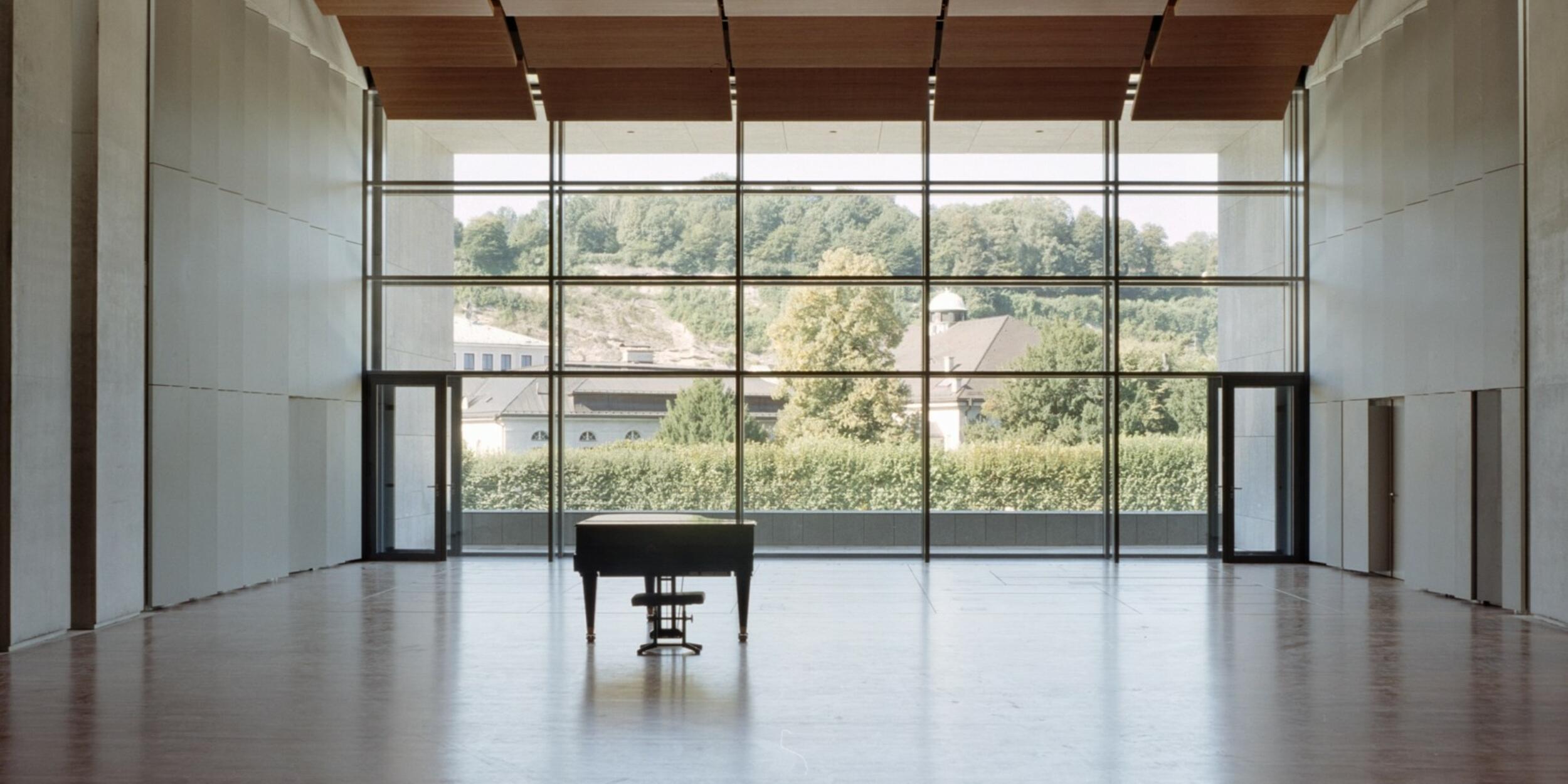 Leerer Solitär, Parkettboden, große Fensterfront, davor ein Piano | © Andrew Phelps